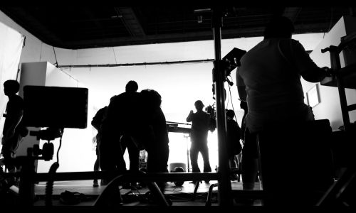 Behind the shooting video production and lighting set for filming which movie crew team working and silhouette shadow of camera and professional equipment in big studio for commercial advertising.